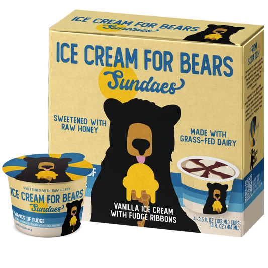 A box and cup of Sundaes 'Ice Cream for Bears' vanilla ice cream with fudge ribbons, shown on a plain white background. The packaging features a tan background with a large black bear holding a yellow ice cream cone and blue text.